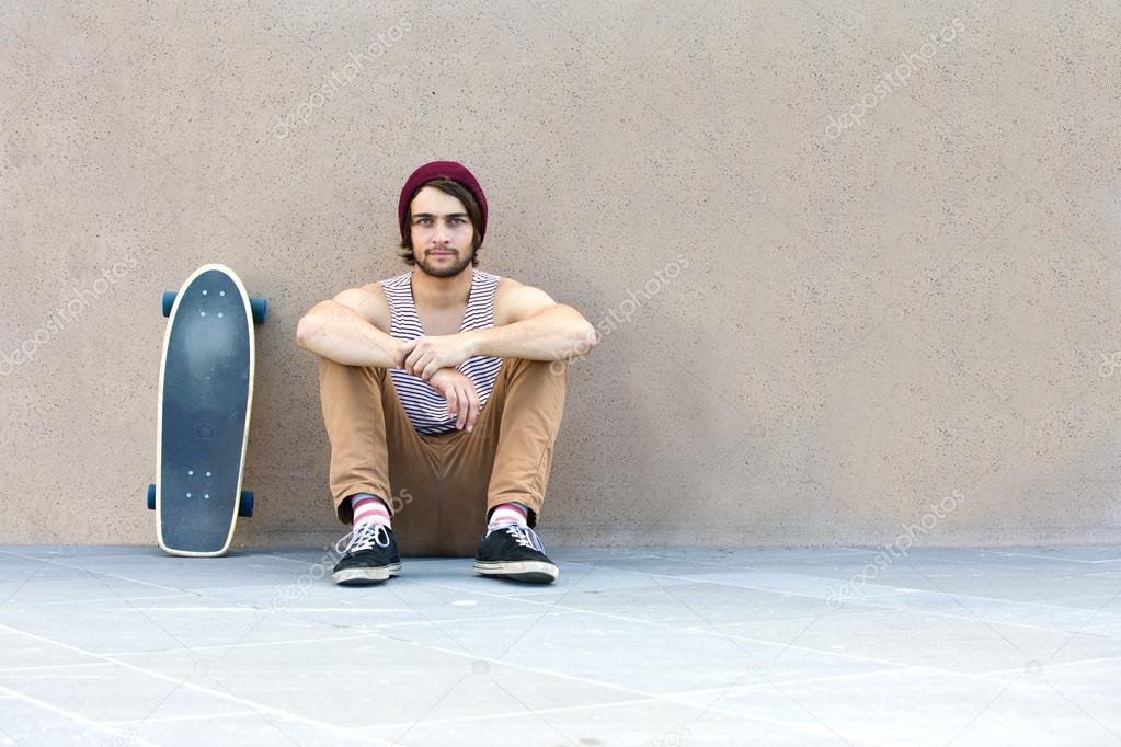 Skateboarder sitting against granite wall
