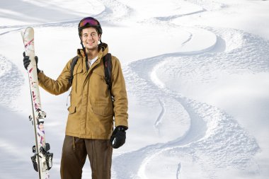 Young off piste skier standing in front of fresh tracks clipart