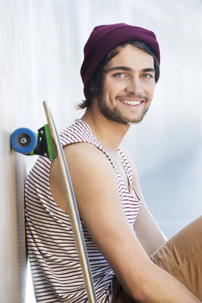 Homem feliz sentado com skate — Fotografia de Stock