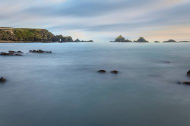 Wide-angle Irish coast with smooth long-exposure water, rugged sea stacks, and a keyhole sea arch on cliffs.