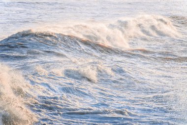Büyük İrlanda Denizi dalgaları, sıcak güneş ışığıyla arka planda, desenli ibikli ibikli, sprey ve çalkantılı kıyı sularını gösterir..