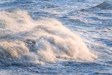 Düşük açılı İrlanda Denizi dalgaları, sıcak güneş ışığıyla aydınlatılan köpüklü sprey, çalkantılı kıyı sularını gösteriyor..