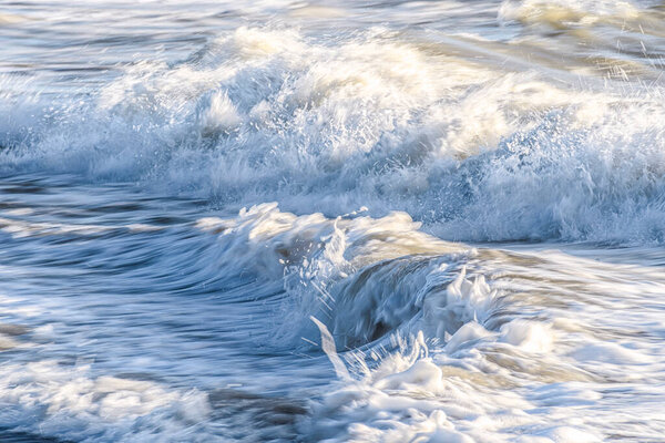 Динамический двухволновой разрыв, светящаяся пена и холодная голубая вода захватывают сырое, высокоэнергетическое прибрежное море.