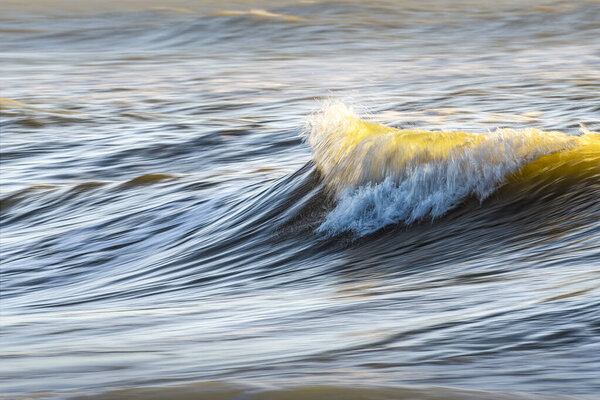 Одинокая, светящаяся волна в Ирландском море, солнечный свет, освещающий гребень и мелкий туман над поверхностью.