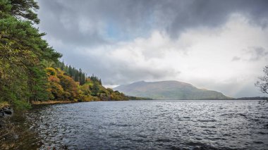 Muckross Gölü 'nün sonbahar ağaçları, Torc Dağı ve koyu yansıtıcı su ile panoramik manzarası, Killarney, İrlanda