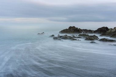 Keskin kaya oluşumlarıyla huysuz İrlanda deniz manzarası ve bulutlu alacakaranlık sahnesinde bulanık gelgit.