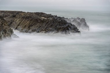 İrlanda Denizi 'nde uzun süre açık denizde uzanan çatlak uçurum dramatik gri ışıkta.