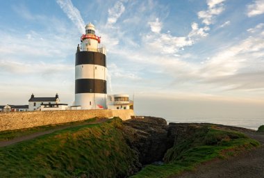 Engebeli kireçtaşı uçurumlarındaki kanca feneri, kış ışığı, yeşil burunlar ve İrlanda kıyılarındaki Atlantik sörfü.