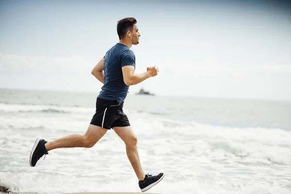 Homem correndo na praia ensolarada — Fotografia de Stock