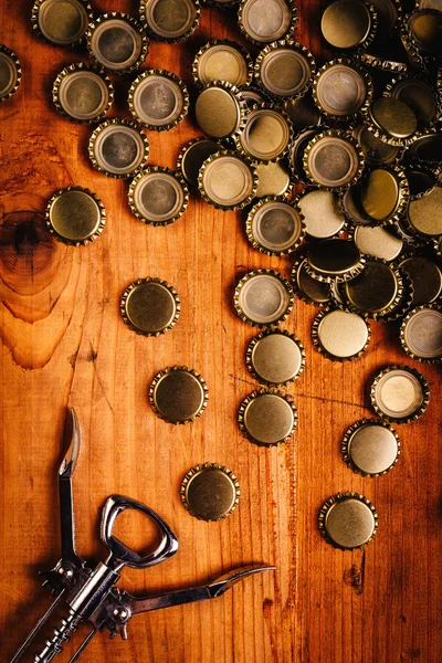 Classic bottle opener and pile of beer bottle caps — Stock Photo, Image