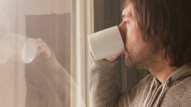 Oturma odasının penceresinden bakan traşsız erkek yakın, kahve içme ve hayatının geri düşünme, yetişkin beyaz adam düşünme