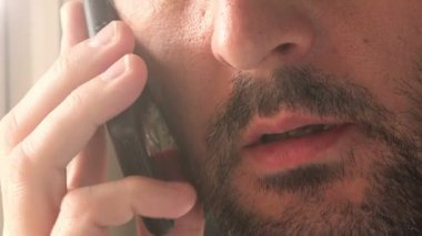 Cep telefonuyla konuşan rahat traşsız adam, oturma odasının penceresinin yanında durarak, yüz görüntülerini kapatın.