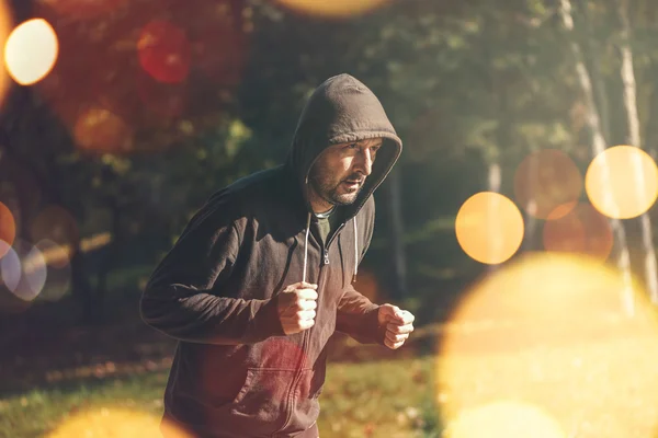 Hombre encapuchado corriendo en el parque en la mañana de otoño — Foto de Stock