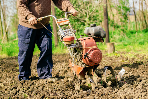 Man preparing garden soil with cultivator tiller