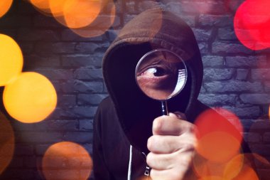 Hooded computer hacker with magnifying glass clipart