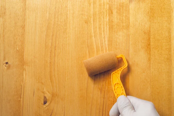 Tangan dengan rol cat menerapkan pernis akrilik di papan kayu — Stok Foto