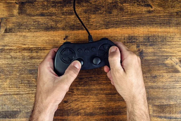 Male gamer using gamepad controller on wooden desk, top view — Stock Photo, Image