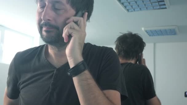 Случайный человек разговаривает по мобильному телефону перед зеркалом — стоковое видео