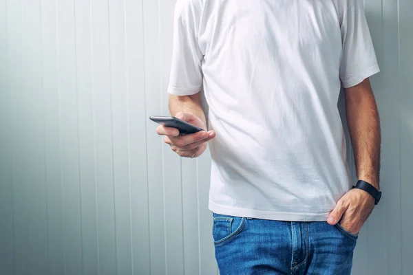 Casual man in wit t-shirt met behulp van mobiele telefoon — Stockfoto