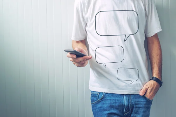 Ragazzo con palloncini vocali stampati sulla camicia usando il telefono cellulare — Foto Stock