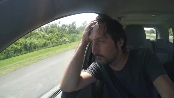 Чоловік їде в машині і дивиться через вікно — стокове відео