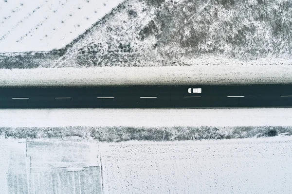 从空中俯瞰公路上的一辆白色小车 穿过冰雪覆盖的冰冻的乡村风景 俯瞰无人驾驶摄影 — 图库照片