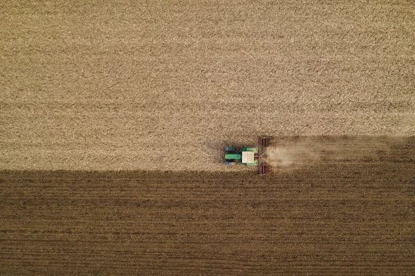 Aerial view of agricultural tractor tilling and harrowing ploughed field, directly above drone pov image of machinery working on farmland