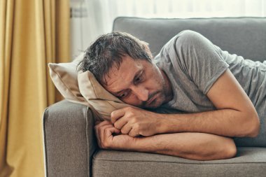 Bunalımlı somurtkan adam oturma odasında tek başına yatıyor ve düşünüyor, yetişkin beyaz erkek orta yaş krizine giriyor.