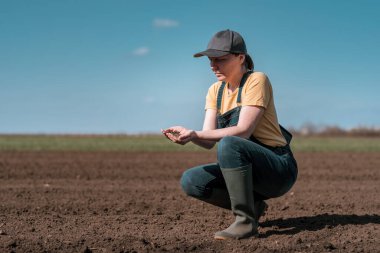 Female farmer agronomist checking the quality of ploughed field soil before sowing season, selective focus clipart