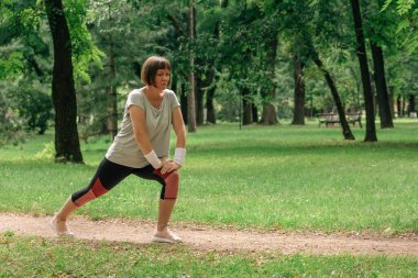 Kadın koşucu kaslarını esnetiyor ve parkta koşmak için ısınıyor, seçici odaklanma