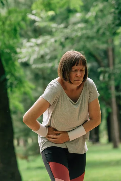 公園で実行中に下腹部の痛みを感じた後 痛みを伴う顔の痛みを持つ女性ジョギング — ストック写真