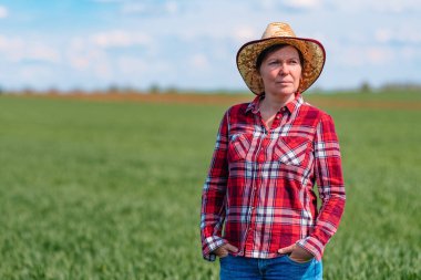 Yeşil buğday tarlasında duran kendine güvenen kadın çiftçinin portresi.