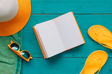 Yaz tatilinde okumak, boş bir kitapla sahil aksesuarlı mavi ahşap tahtalar ve düz manzaralı sayfalar.
