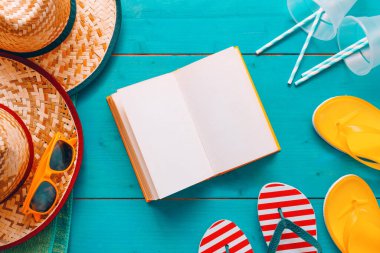 Yaz tatilinde okumak, boş bir kitapla sahil aksesuarlı mavi ahşap tahtalar ve düz manzaralı sayfalar.