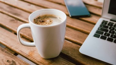 Laptop bilgisayarı ve cep telefonu olan kahve fincanı serbest çalışanların masasında, seçici odaklı.