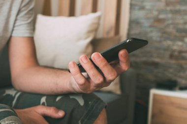 Evde cep telefonu kullanan sıradan erkek eli kapalı oturma odasında özel, seçici odaklı.