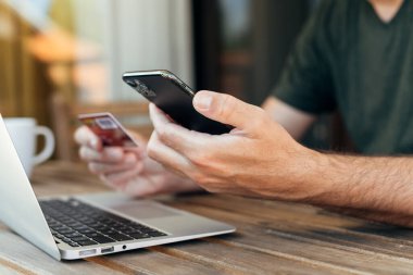 Ev balkonundan online alışveriş, dizüstü bilgisayar, cep telefonu ve kredi kartı kullanan bir adam internetten eşya alıyor, seçici odaklı.