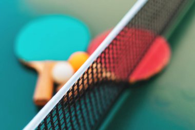 Masa tenisi raketleri ve yeşil masa yüzeyindeki pinpon topları net ve seçici odaklı.