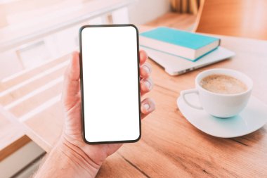 Boş cep telefonu akıllı telefon ekran modeli. Elinde kahve fincanı, dizüstü bilgisayarı ve ev ofisinde kitap olan akıllı telefonu elinde tutan adam.
