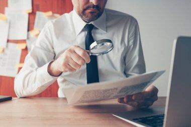 İş adamı ofis masasında büyüteçle belge sözleşmesi kağıtlarını okuyor, seçici bir odaklanma ile kapatıyor.