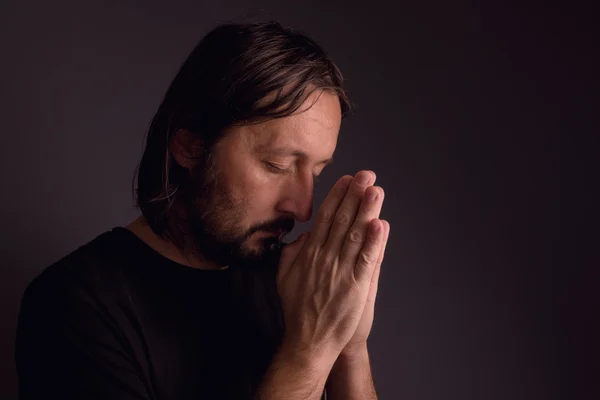 Взрослый бородатый мужчина молится в темной комнате — стоковое фото