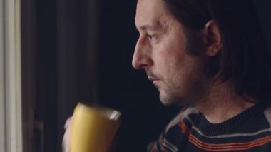 Yetişkin beyaz adam rahatlatıcı ve pencereden dışarı bakıyor çay içme
