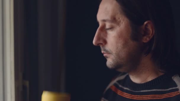 Mid adult caucasian man relaxing and drinking a cup of tea, looking out of window — Stock Video