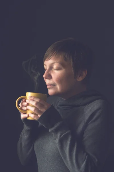 Vacker kvinna att lukta hett kaffe i mörkt rum — Stockfoto