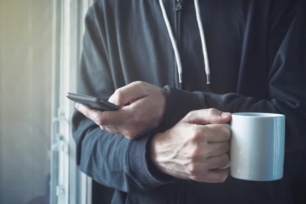 Boire du café et envoyer des SMS avec téléphone portable le matin — Photo