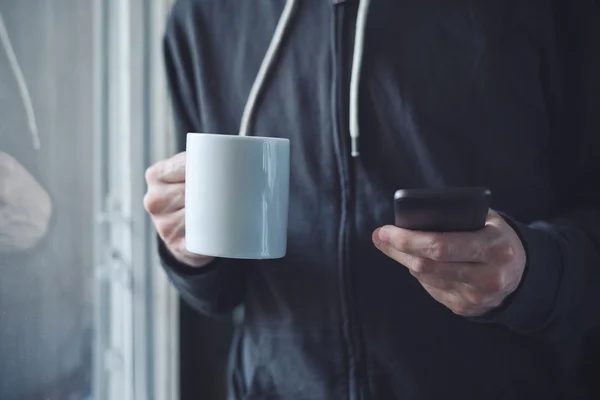 Boire du café et envoyer des SMS avec téléphone portable le matin — Photo