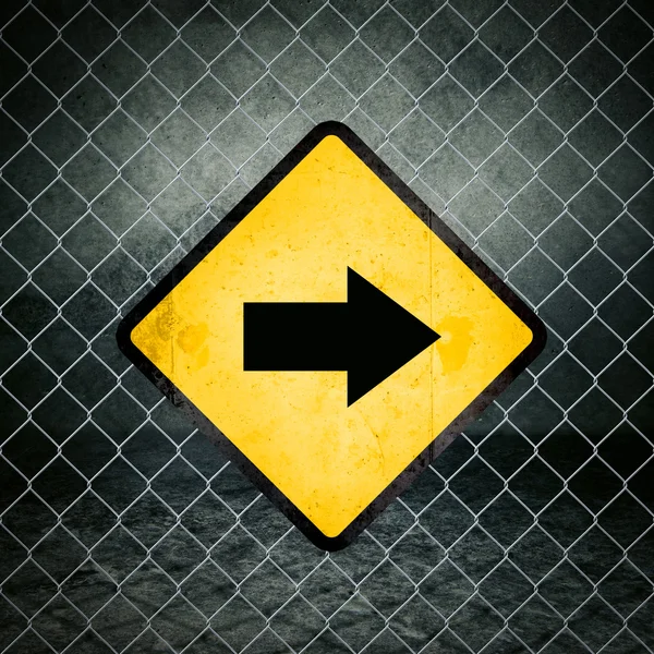 Señal de advertencia amarilla Grunge de dirección correcta en la valla de enlace de cadena — Foto de Stock