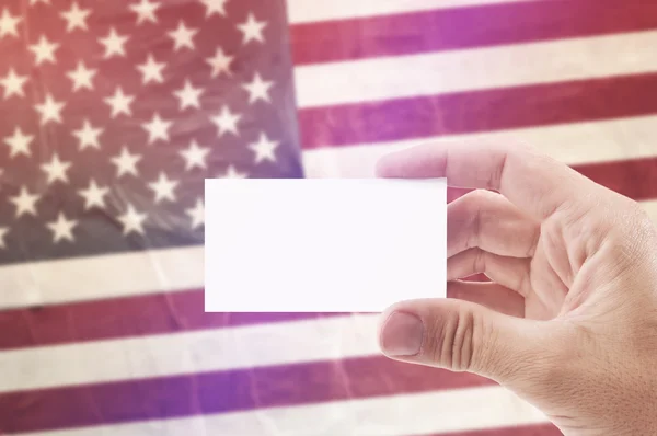 Hombre con tarjeta de visita en blanco contra la bandera nacional de EE.UU. — Foto de Stock