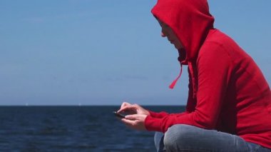 Okyanus iskelede mobil akıllı telefon kullanan genç kadın