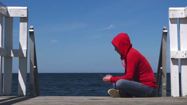 Ung kvinna med smarta mobiltelefon på ocean pier — Stockvideo
